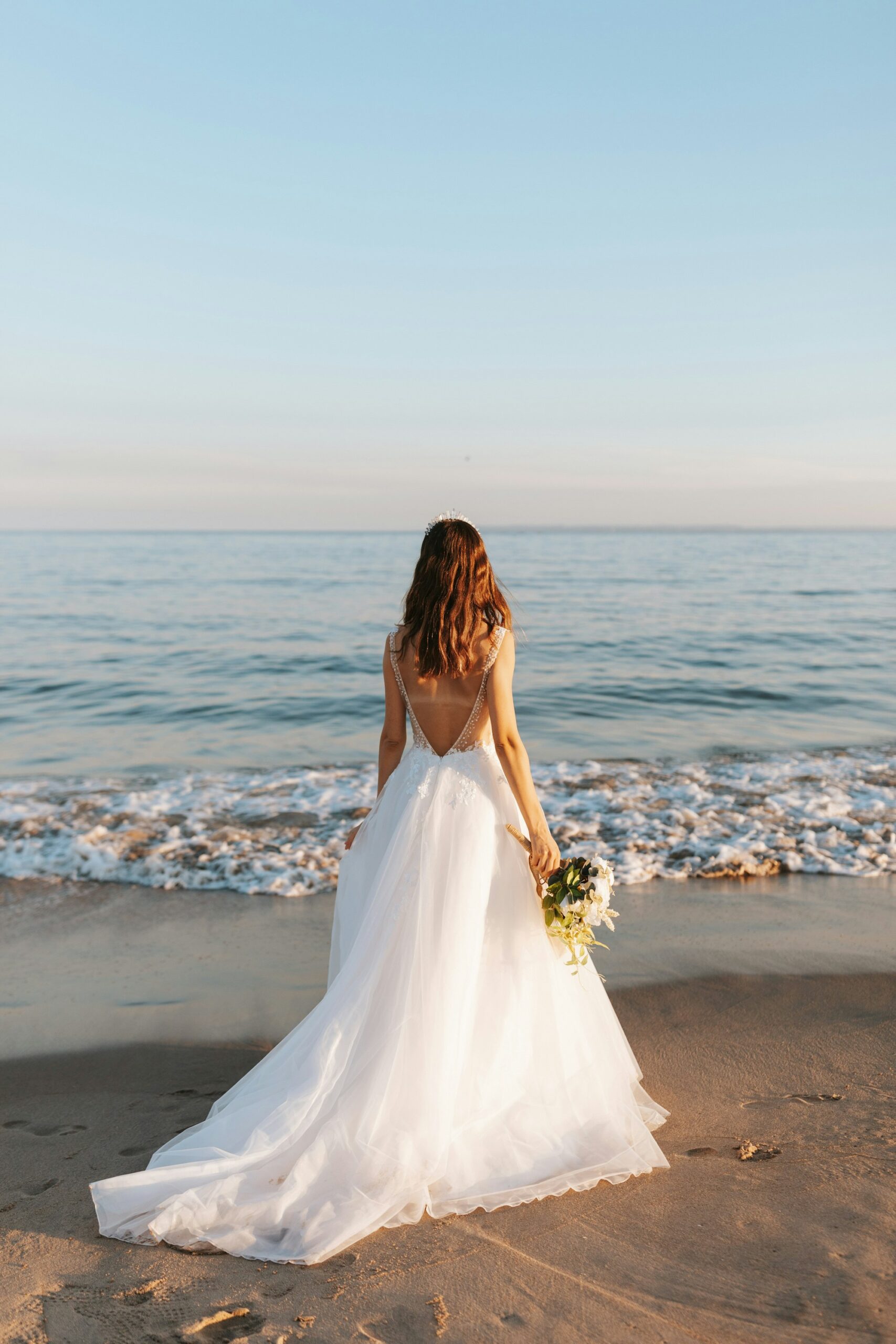 Bride in a flowing gown looking out at the ocean
